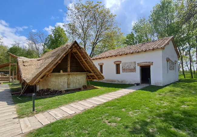Replika drevenej germánskej zemnice s trstinovou strechou vľavo a kamenného kúpeľa s rímskou strešnou krytinou vpravo (foto V. Varsik).